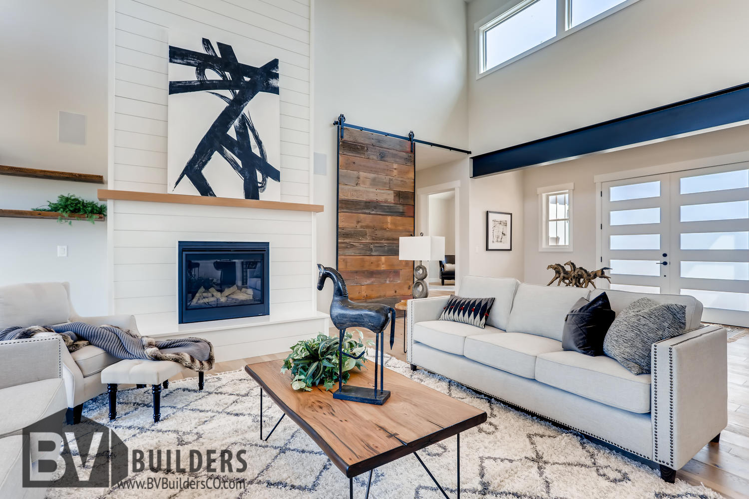 Modern farmhouse great room living room with exposed steel beams, reclaimed wood barn door and shiplap fireplace