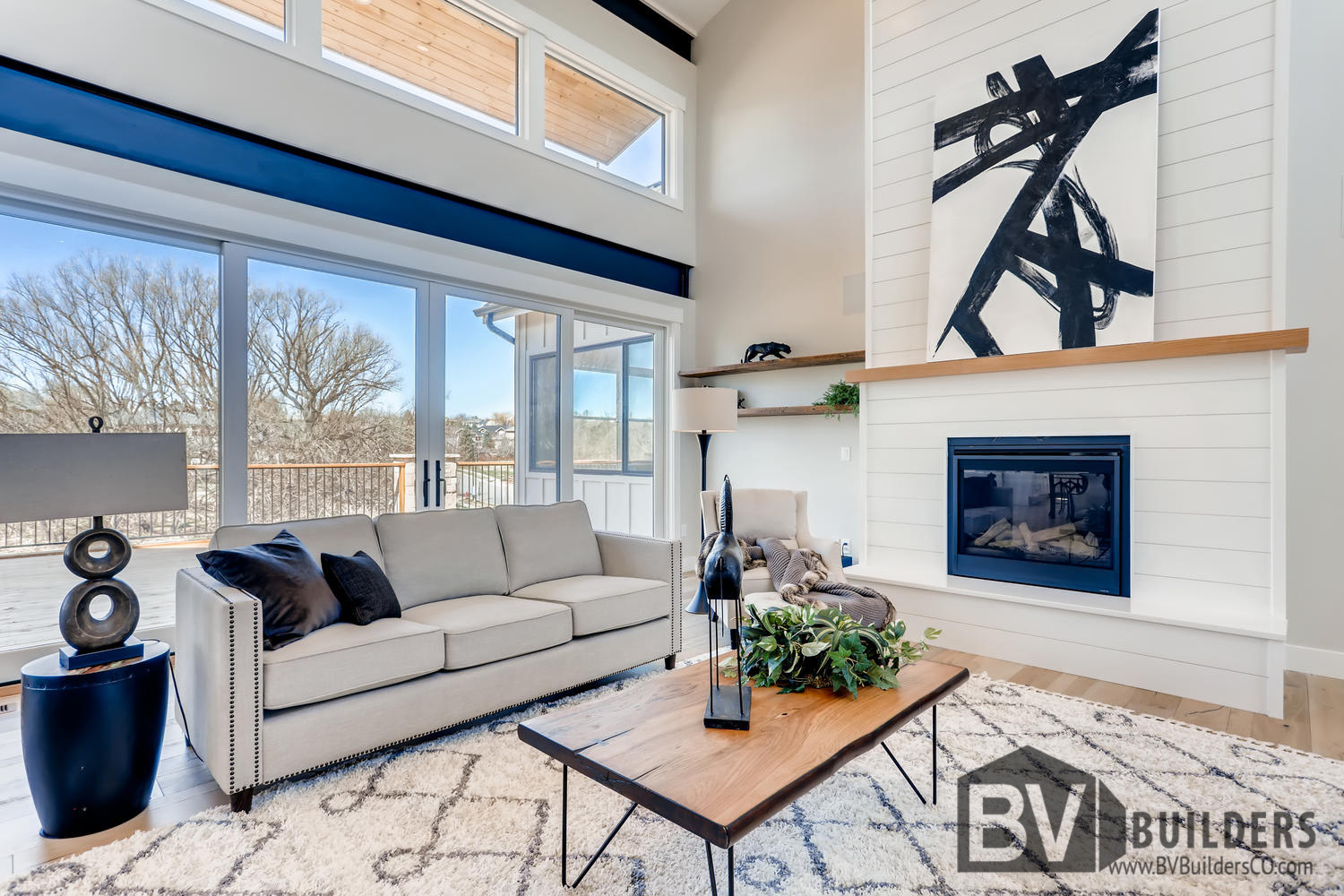 Modern farmhouse great room living room with exposed steel beams, floating shelves, shiplap fireplace and large sliding glass doors