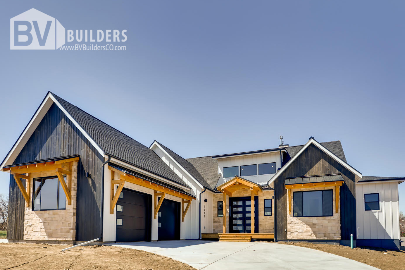 Modern farmhouse exterior with timber framed shed roofs and Coronado stone accent walls. Black front door. Black Garage doors.