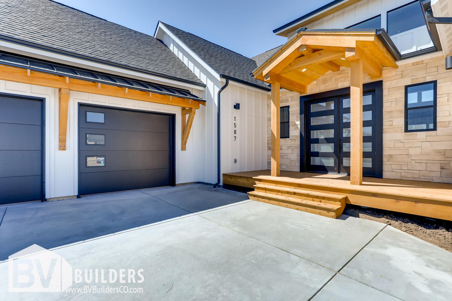 Modern farmhouse front porch with timber framed entry roof, Coronado stone wall, black front door and timber framed shed roof over garage. Black garage doors.